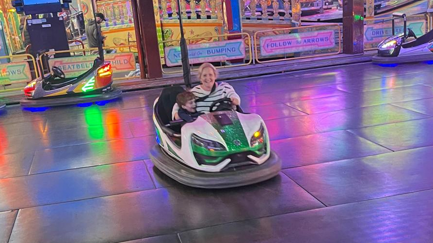 Woman in striped jumper sits in white dodgem car with boy in navy t-shirt cuddled into her side.